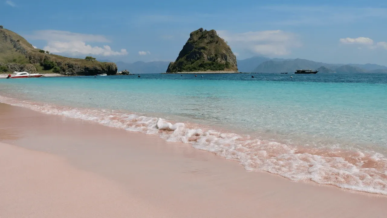 Pink beach with clear water under a blue sky.