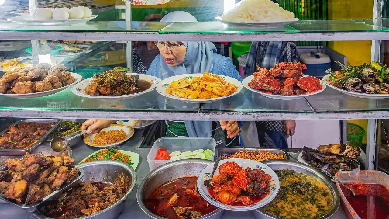 Woman in hijab serving customers food in a traditonal warung